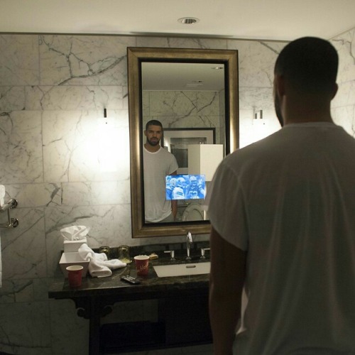 Drake watching a football game projected onto his hotel mirror. Tim Horton's cups litter the counter.